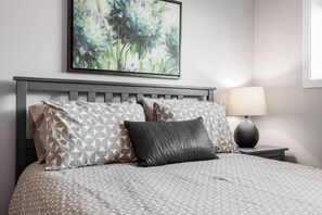 A neatly made bed with patterned bedding, a wall-mounted abstract painting, and a bedside lamp. - Located next to Knox Mountain. Two bedrooms one bathroom peaceful great location (Kelowna)