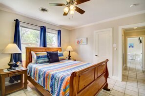 Ein Schlafzimmer mit einem hölzernen Bett, zwei Nachttischen mit Lampen, einem Deckenventilator, einem Fenster mit Vorhängen und einer Tür zu einem anderen Raum.