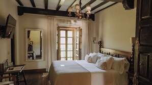 Un dormitorio con una cama grande, un cabecero de madera, una lámpara de araña, un espejo y una ventana con cortinas.