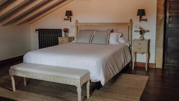 A bedroom with a large bed, a bench, two bedside tables with lamps, a radiator, and a wooden ceiling.
