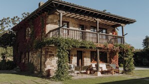 Un edificio de piedra con balcón, mobiliario exterior y jardín.