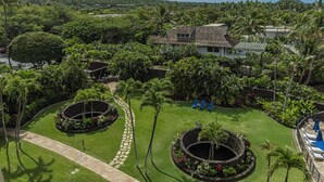 A lush garden with a stone pathway, a circular water feature, and a house with a tiled roof. - Beachfront 2BR condo in Wailea w/ pool and hot tub (Wailea)