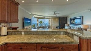 A kitchen with granite countertops, wooden cabinets, and a view to an outdoor patio. - Beachfront 2BR condo in Wailea w/ pool and hot tub (Wailea)