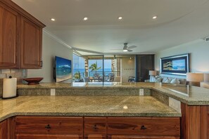 A kitchen with granite countertops, wooden cabinets, and a view to an outdoor patio. - Beachfront 2BR condo in Wailea w/ pool and hot tub (Wailea)