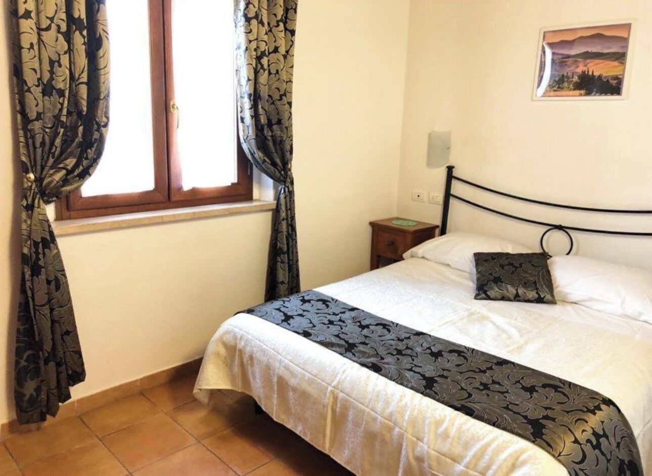 Un dormitorio con cama, cortinas, mesita de noche, un cuadro en la pared y una ventana.