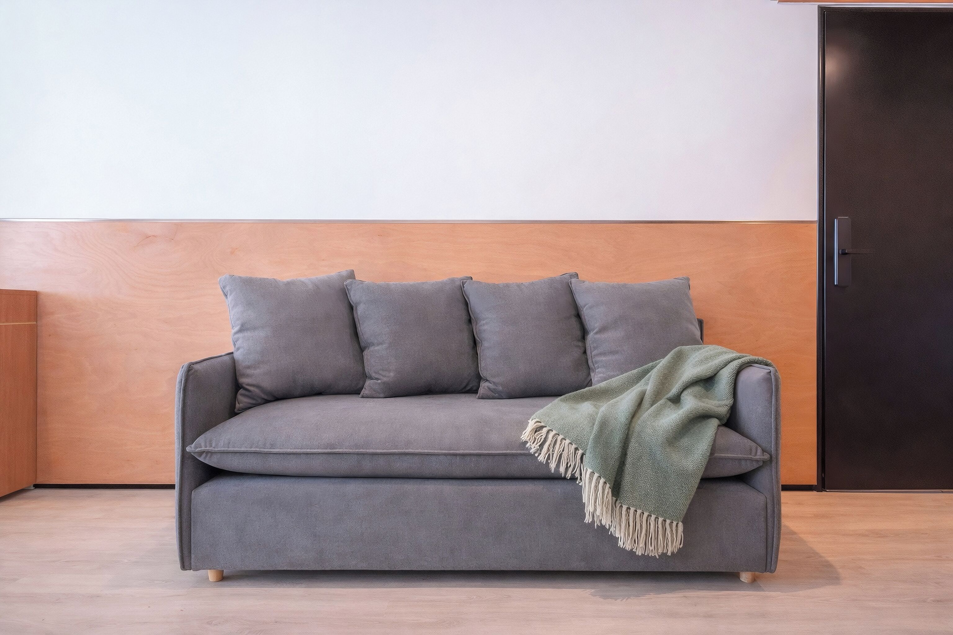 A grey sofa with cushions and a green throw blanket, a wooden headboard, and a dark door.
