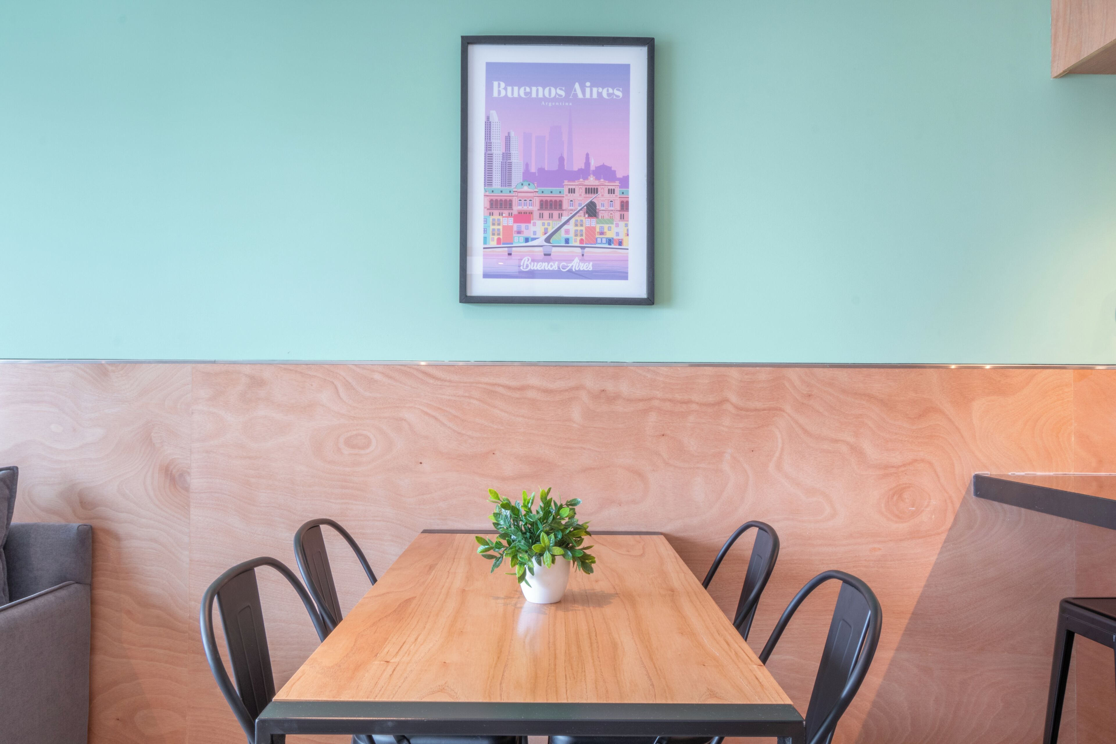 A dining area with a wooden table, four chairs, a potted plant, and a framed cityscape poster on the wall.