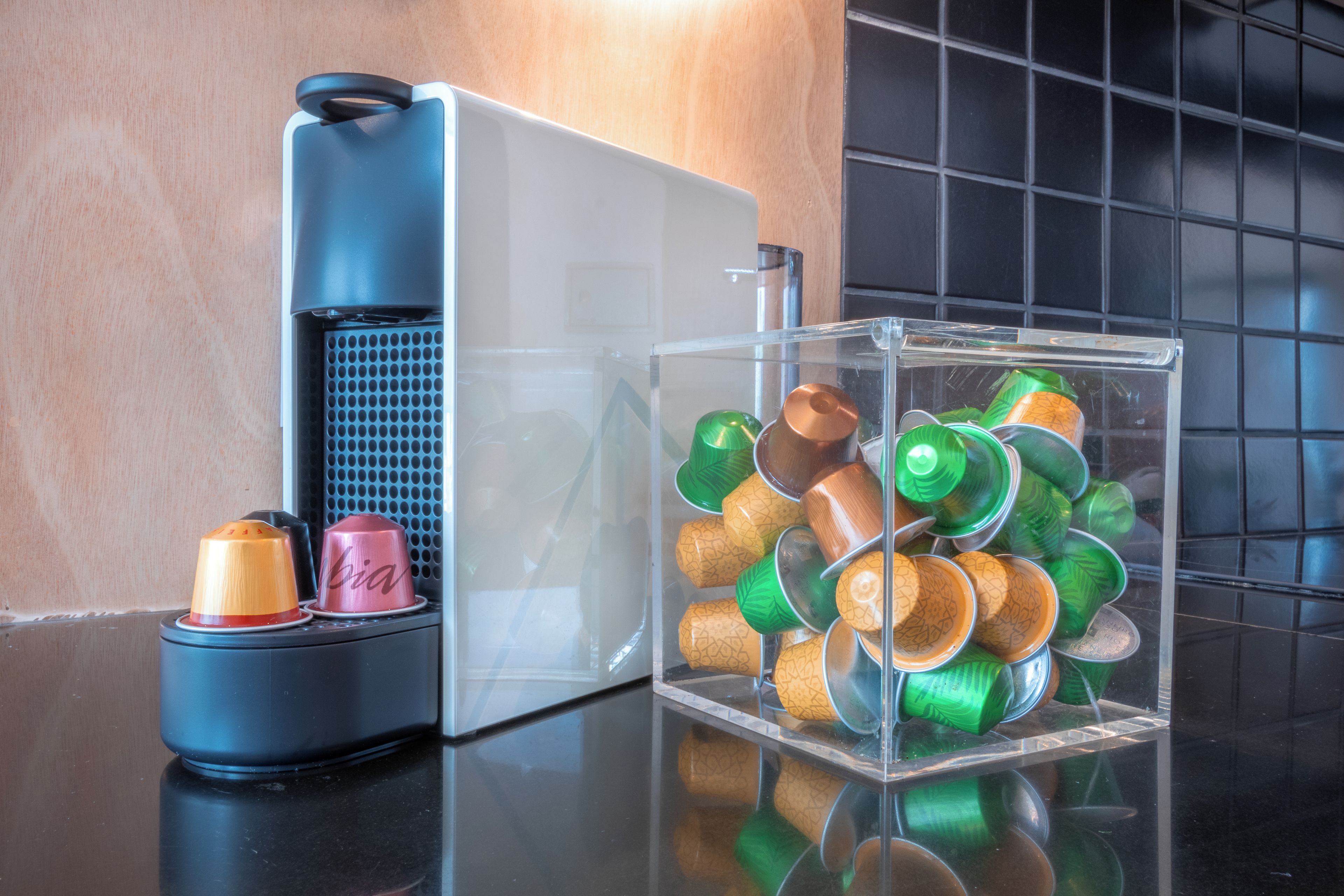 Una cafetera y un recipiente transparente con tazas y platillos variados.