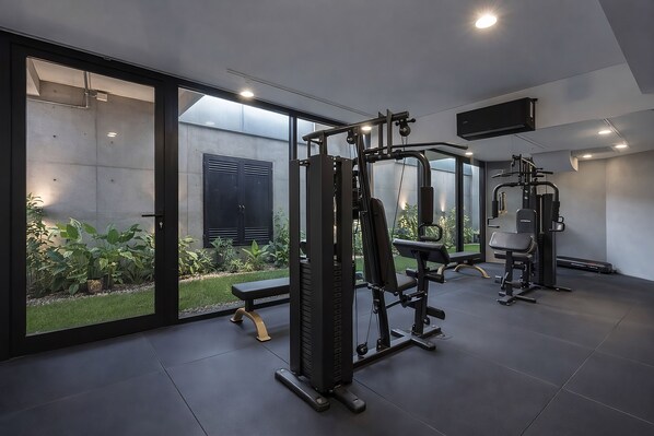 A modern gym with exercise equipment, large windows, and a view of a garden.