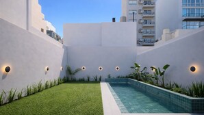 Edificio moderno con piscina, rodeado de vegetación y paredes blancas.