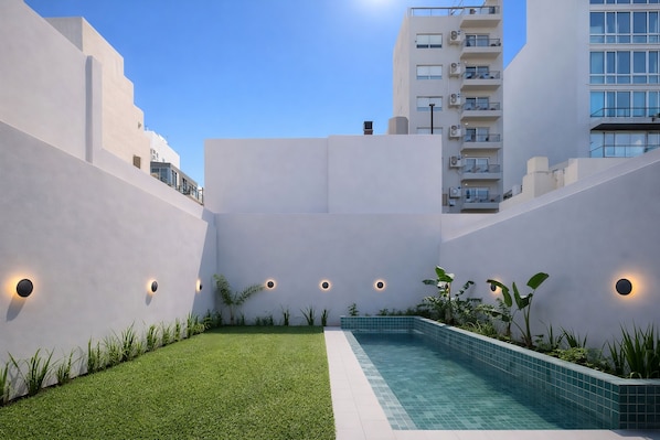 Edificio moderno con piscina, rodeado de vegetación y paredes blancas.