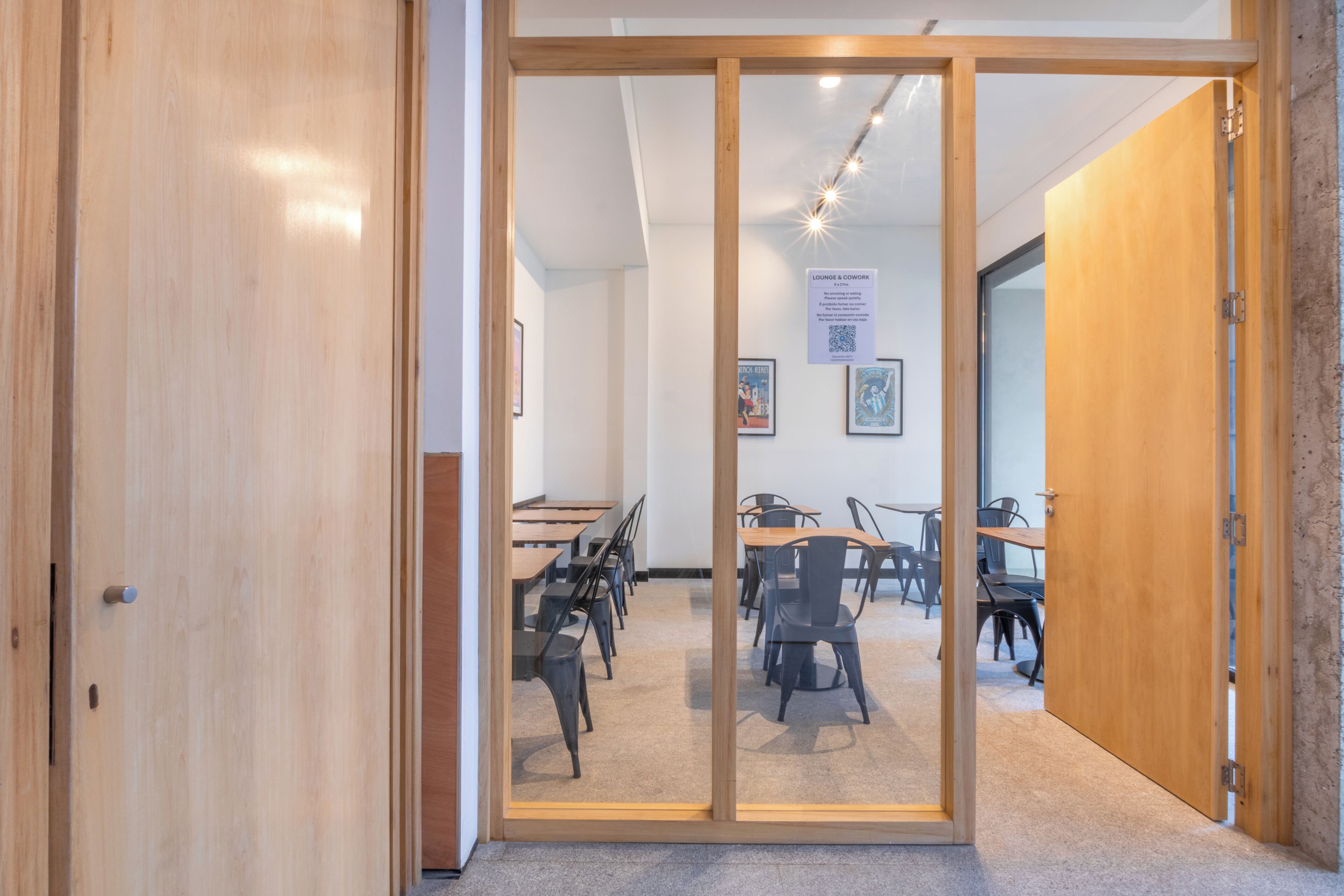 Una habitación con puerta de cristal que da a un comedor con mesas y sillas.