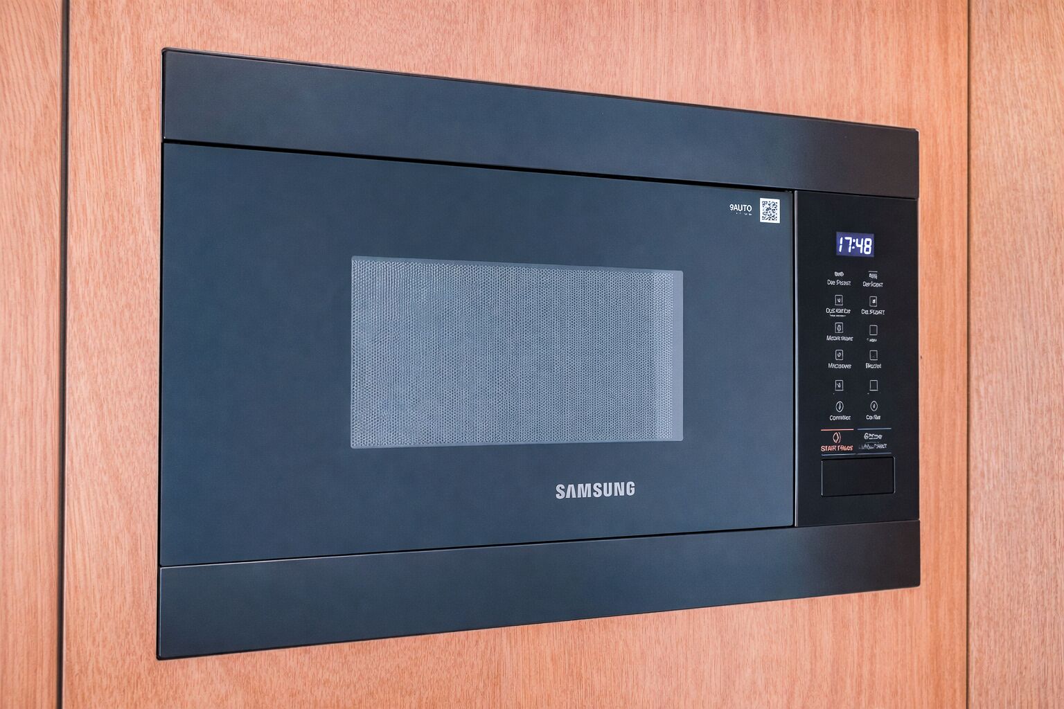 En Samsung-mikrovågsugn med en digital display, en kontrollpanel och en klistermärke med en QR-kod.