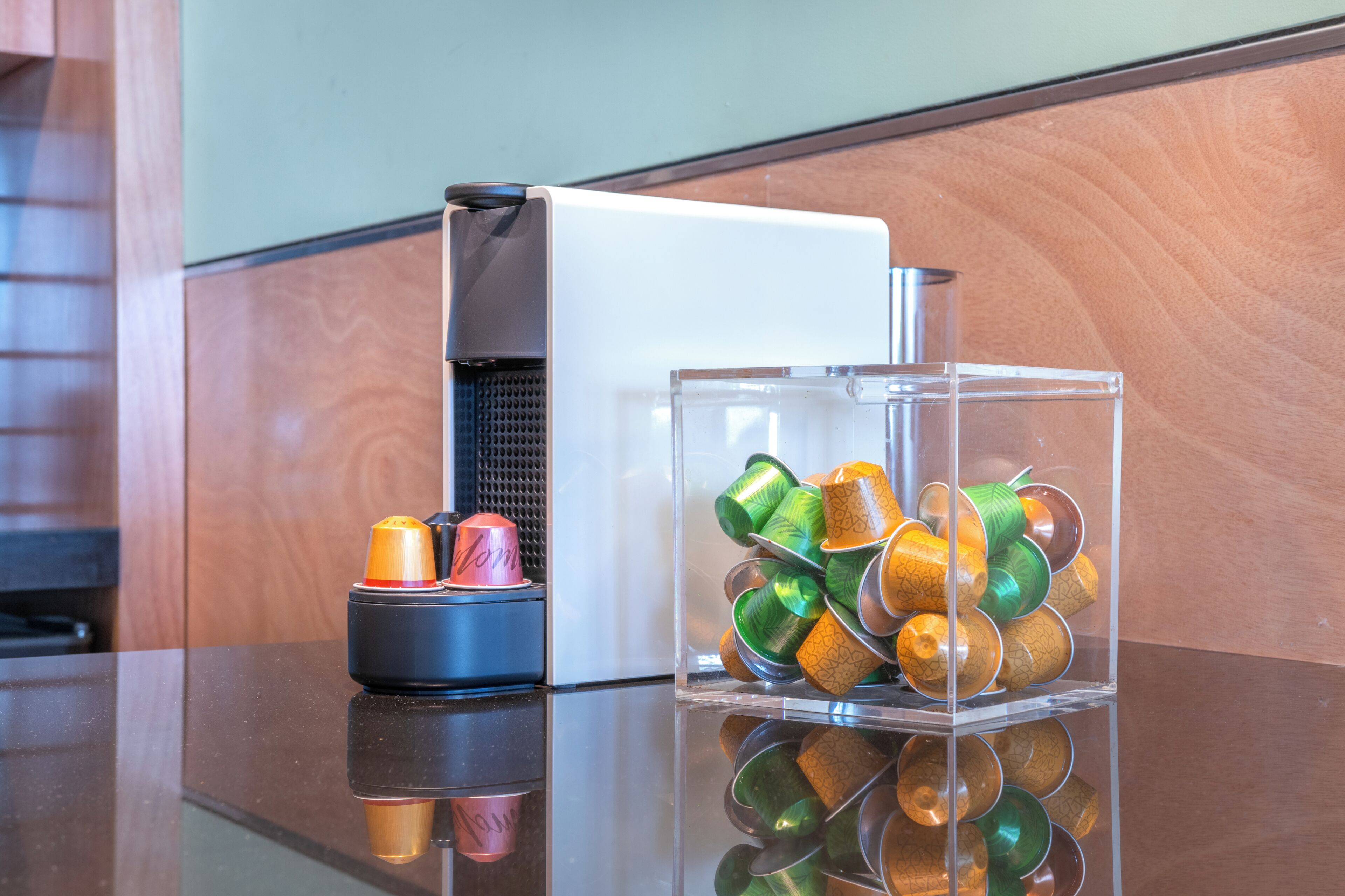 Une machine à café et un récipient en verre contenant des tasses colorées, le tout posé sur une surface réfléchissante.