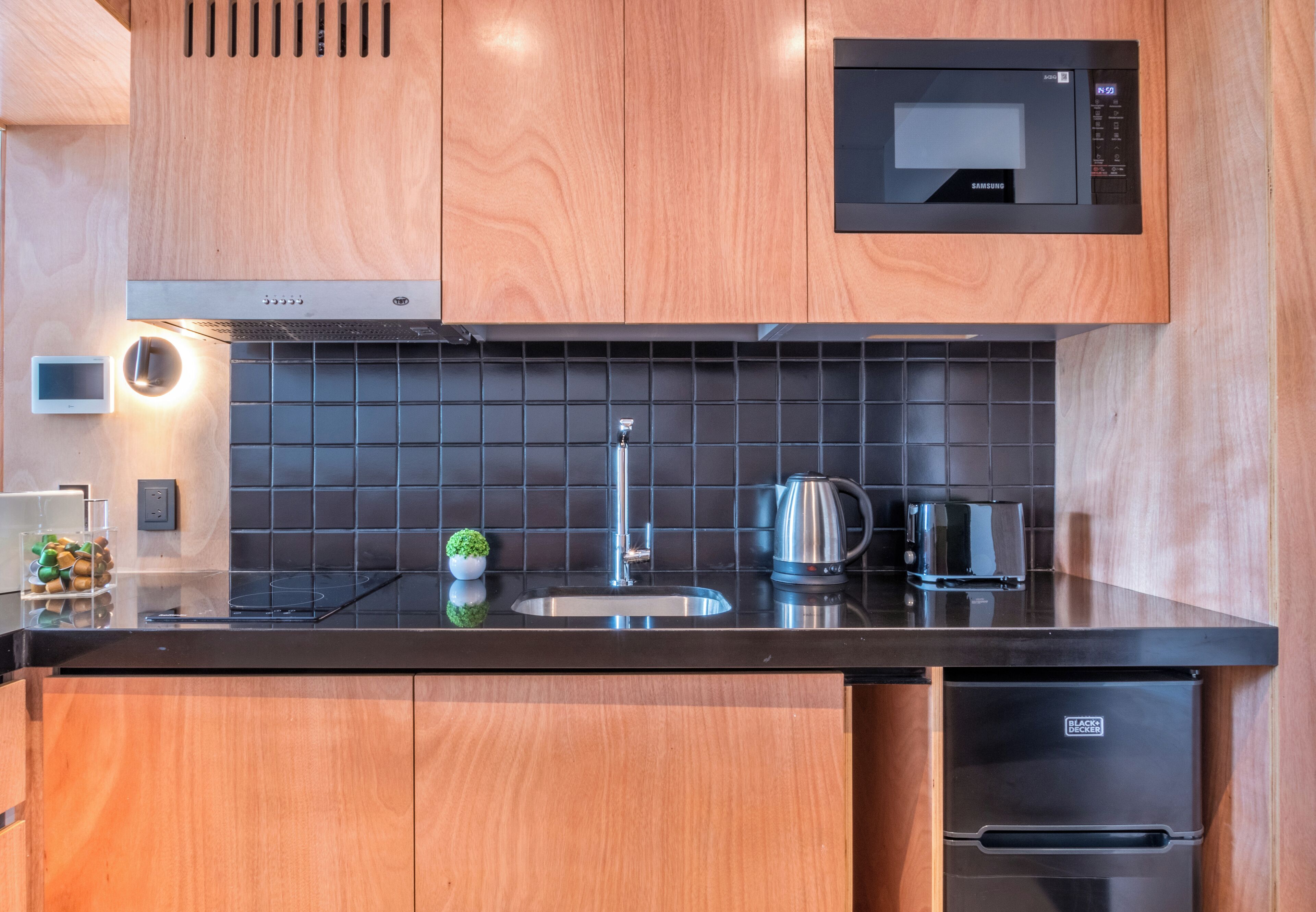 Une cuisine moderne avec des meubles en bois, un plan de travail noir, un four à micro-ondes encastré, une bouilloire et un lave-vaisselle.