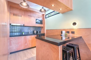 A modern kitchen with wooden cabinetry, a black countertop, and two bar stools. - Trendy Apartments in Palermo Hollywood by BueRentals (Buenos Aires)