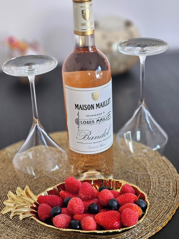 A bottle of Maison Maillet brandy with a label, two wine glasses, and a bowl of berries.