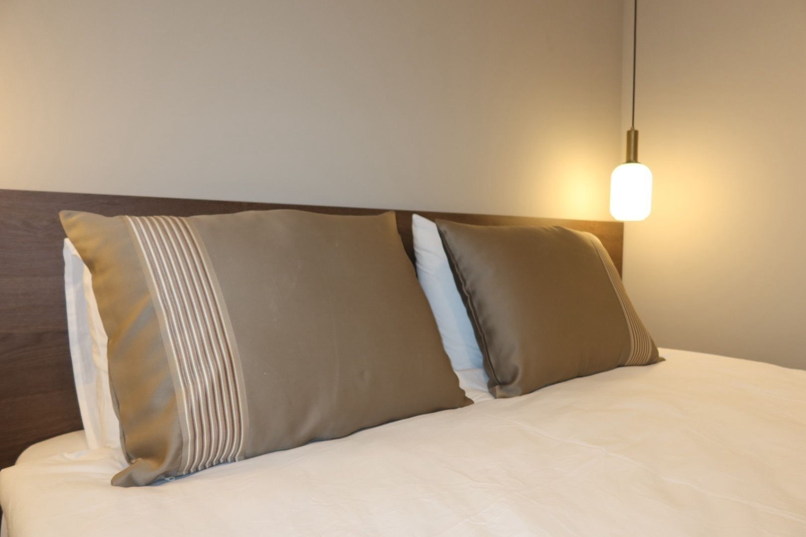 A bed with two pillows, a headboard, and a wall-mounted light fixture.