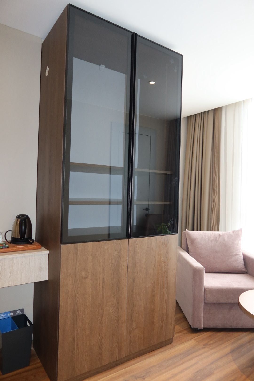 Une pièce comprenant une armoire en bois, une petite table avec une bouilloire, un canapé et une poubelle.