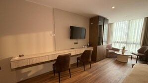 Habitación de hotel con piso de madera, televisor de pantalla plana en la pared, escritorio con silla, sofá y mesa de centro.