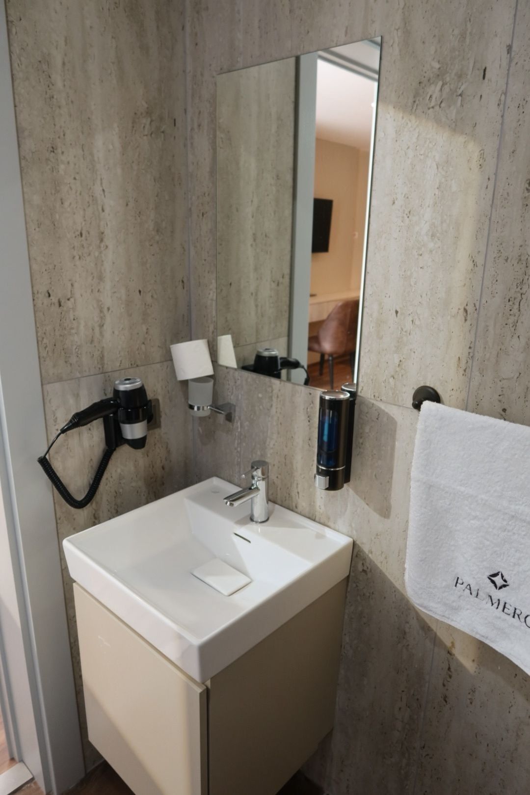 A bathroom with a white sink, a mirror, a towel rack, and a towel with 'PALMER' text.