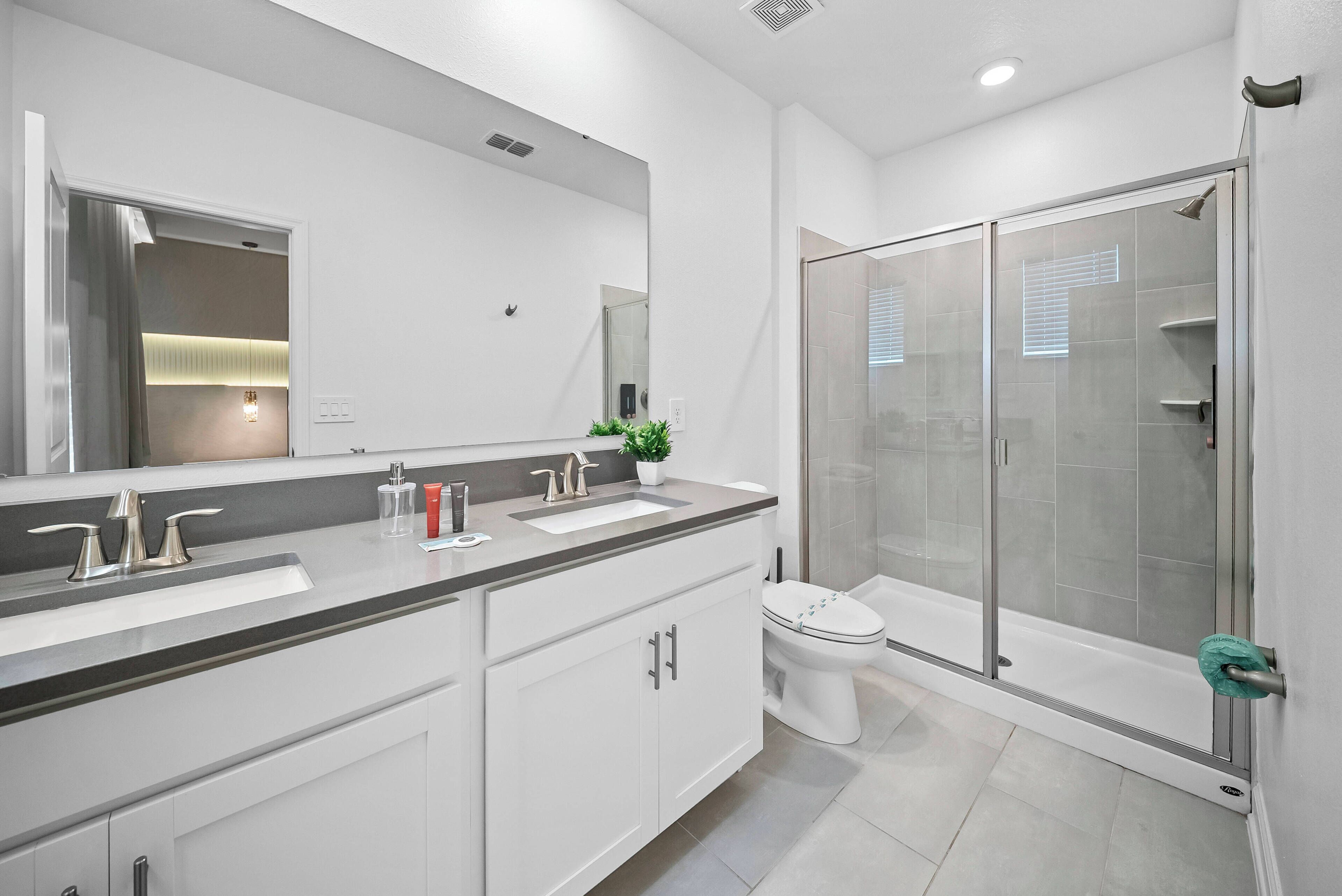 Enjoy a bright and airy bathroom with sleek gray countertops and white cabinetry for a modern feel. The spacious glass shower invites relaxation, and a large mirror enhances natural light for a refreshing start to your day.