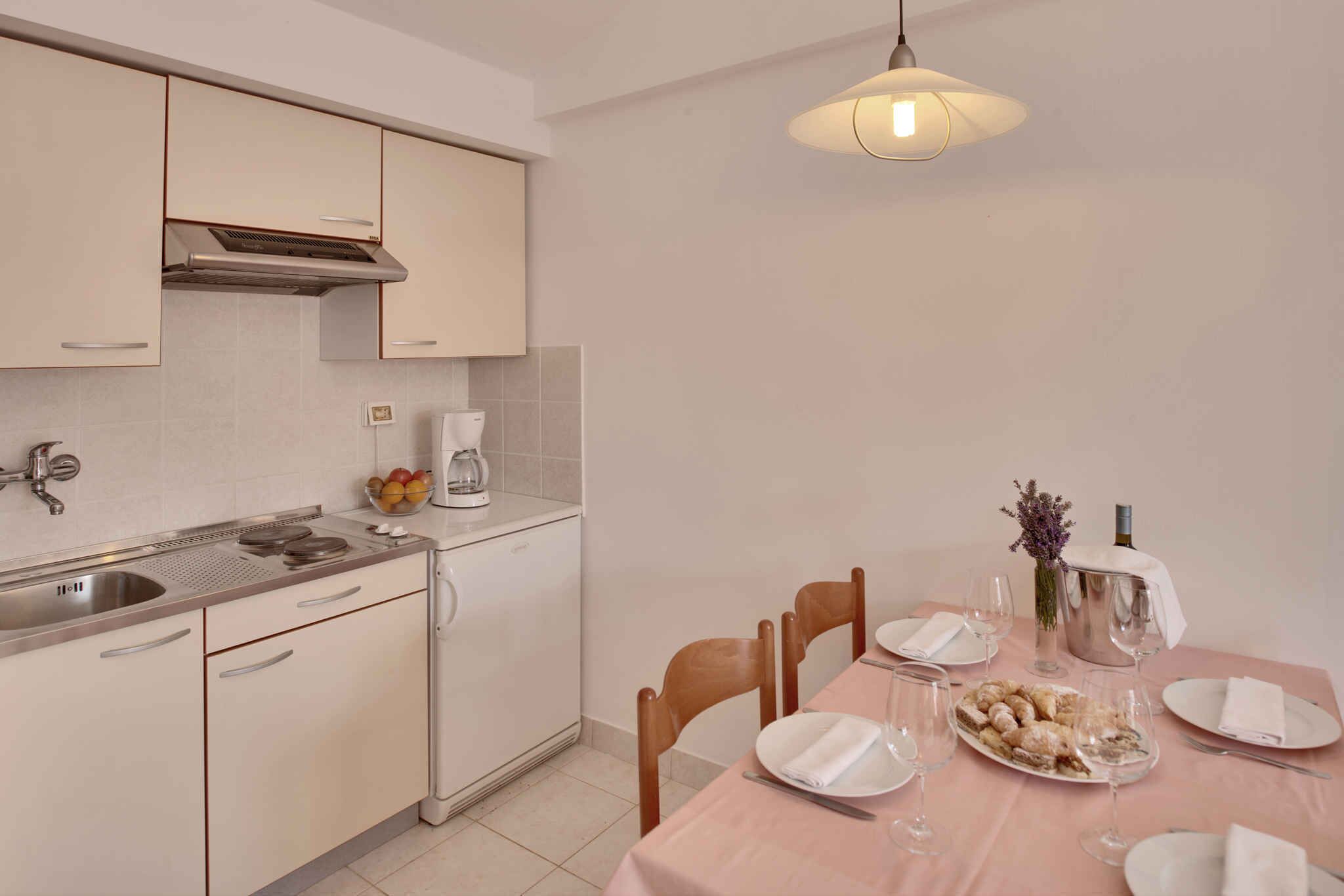 Une cuisine moderne avec un coin repas, des appareils en acier inoxydable et une table dressée pour deux personnes, avec des verres à vin et un vase de fleurs.
