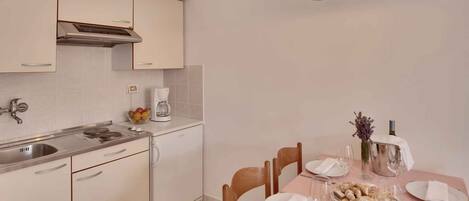Une cuisine moderne avec un coin repas, des appareils en acier inoxydable et une table dressée pour deux personnes, avec des verres à vin et un vase de fleurs.