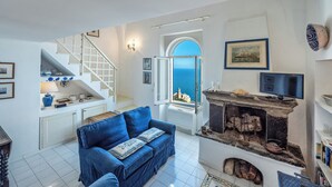 A compact living space with a sofa, a fireplace, a television, and a view of the sea through a window. - Casa Capo di Conca by Wonder Tour (Conca dei Marini)