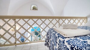 A bedroom with a bed, a balcony with a lattice railing, and a view of a blue-domed building. - Casa Capo di Conca by Wonder Tour (Conca dei Marini)