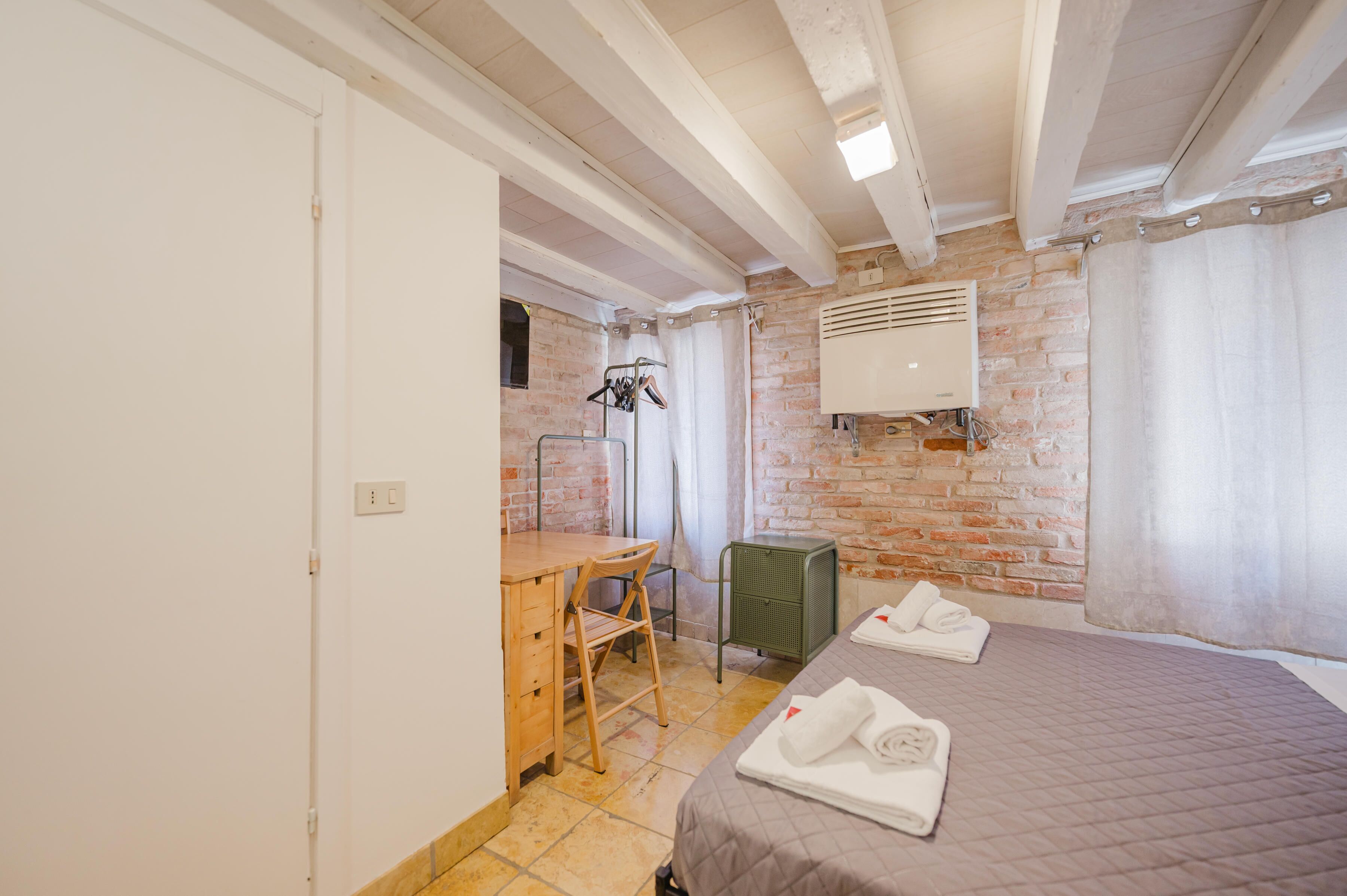 Una habitación con pared de ladrillo, cama con toallas, escritorio con silla y radiador.
