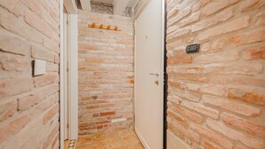 A narrow hallway with exposed brick walls and a tiled floor. - Balastro Design Rooms (Venice)