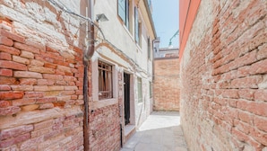 A narrow alleyway with brick walls and a tiled floor, leading to a building entrance. - Balastro Design Rooms (Venice)