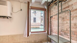 A room with a window, a metal shelf, and a brick wall. - Balastro Design Rooms (Venice)