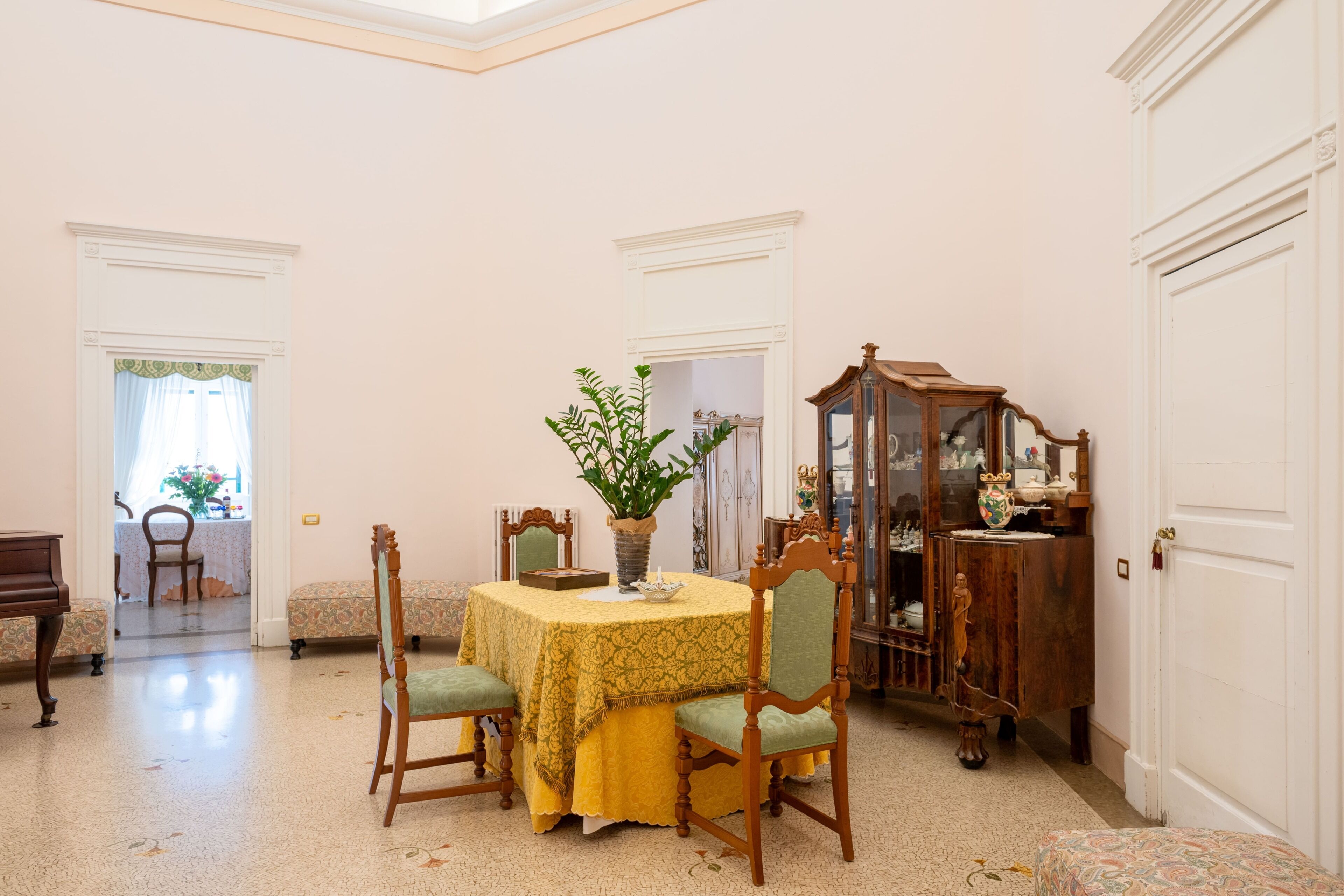 Un comedor con una mesa, sillas, un florero con plantas, un armario de madera y una puerta.