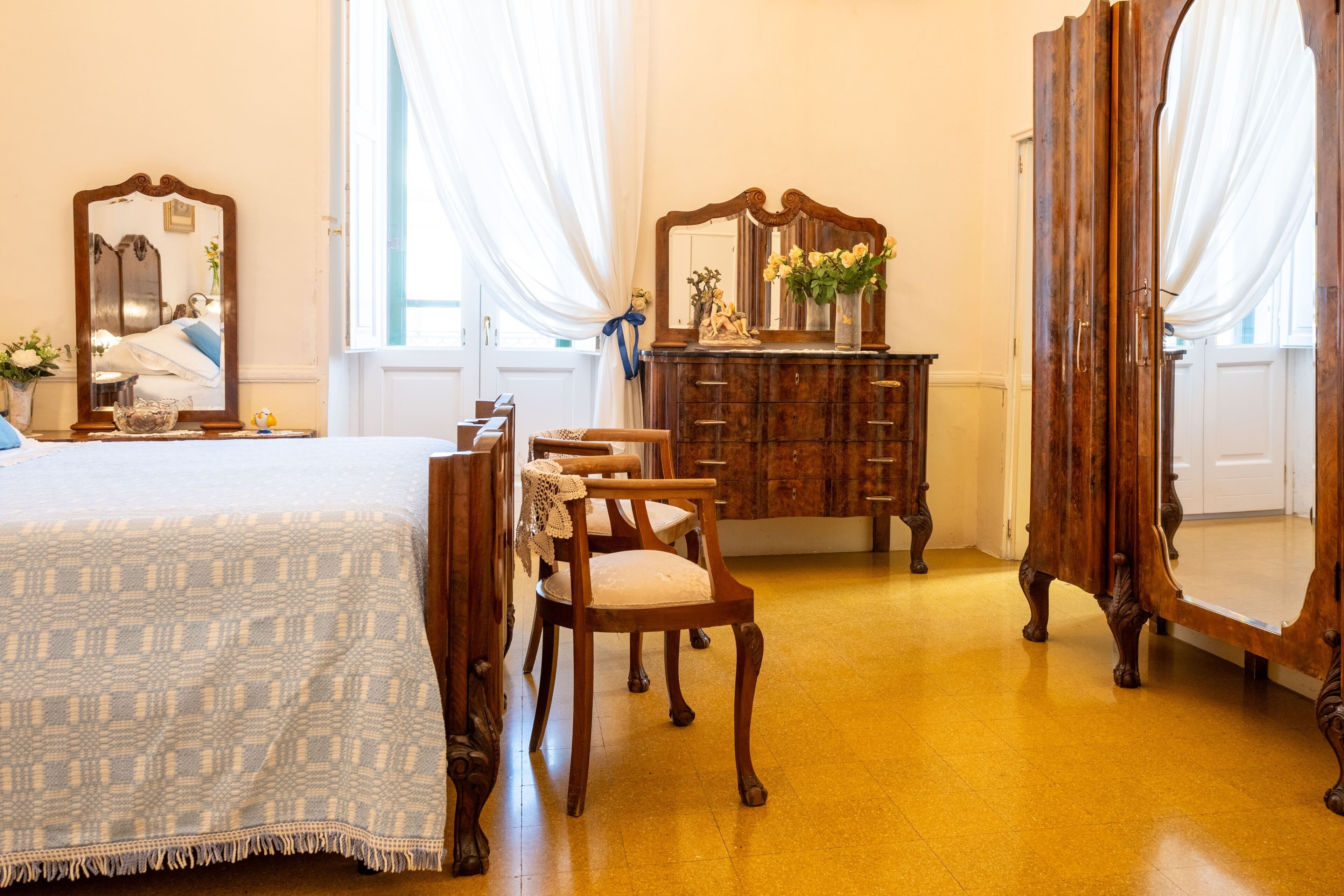 Ein Zimmer mit einem Bett, einem Holzkommode, Stühlen und einem großen Spiegel.