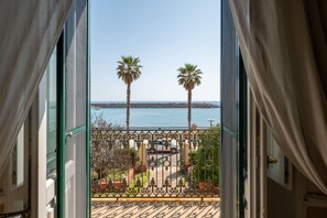 A balcony with a view of the sea, palm trees, and a parked car. - Hotiday Leuca Porto (Santa Maria di Leuca)