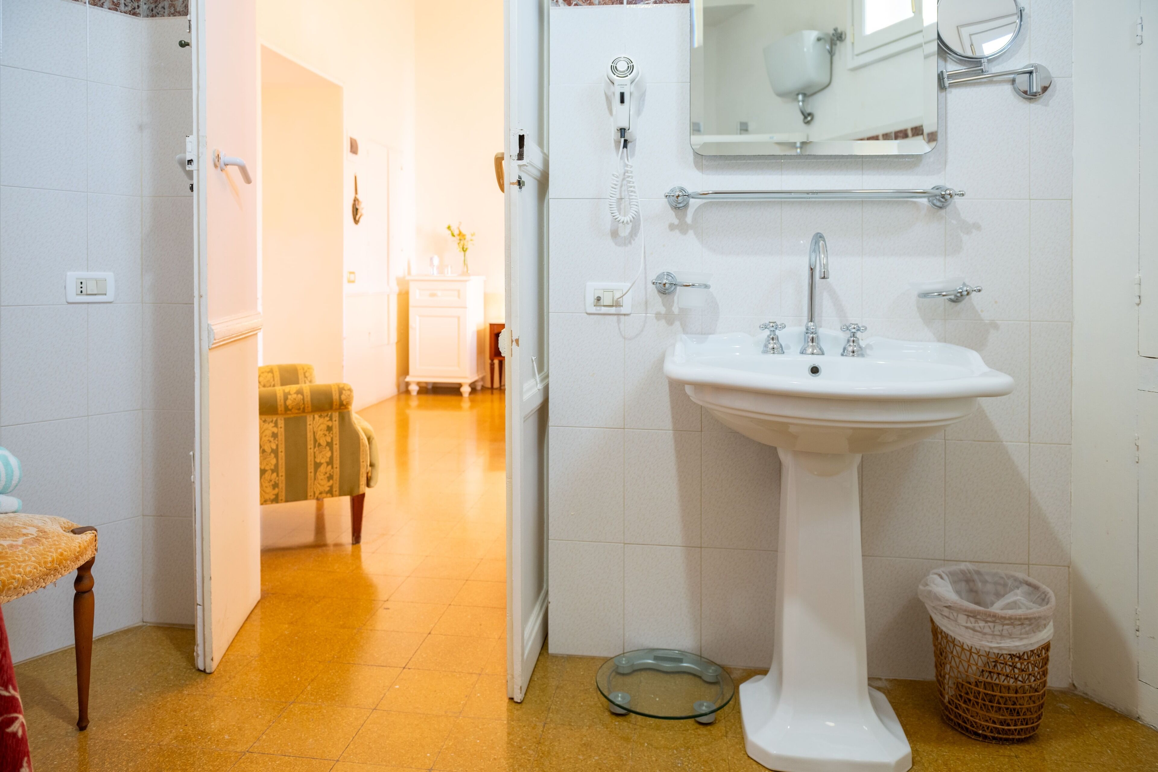 Ein Badezimmer mit einem weißen Waschbecken, einem Spiegel, einem Fön und einem Mülleimer.