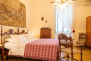 A bedroom with a bed, wooden headboard, a chair, a dresser, a painting on the wall, and a window with curtains. - Hotiday Leuca Porto (Santa Maria di Leuca)