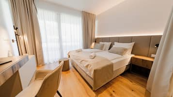 Ein Hotelzimmer mit einem Bett, Nachttisch, Sessel, Schreibtisch und einem großen Fenster mit Vorhängen.