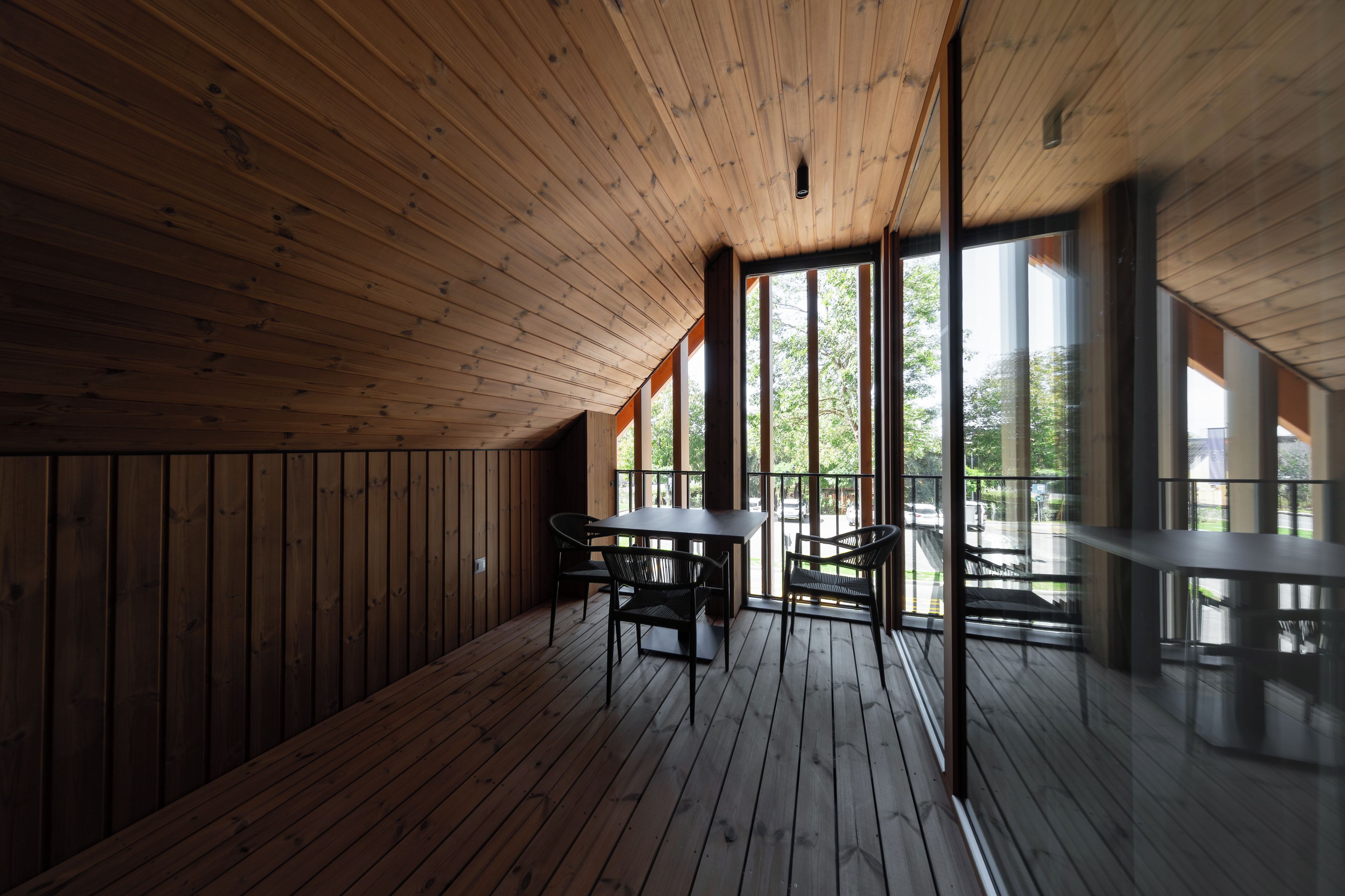 A wooden interior with a high ceiling, large windows, and a table with chairs.