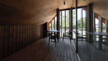 A wooden interior with a high ceiling, large windows, and a table with chairs.