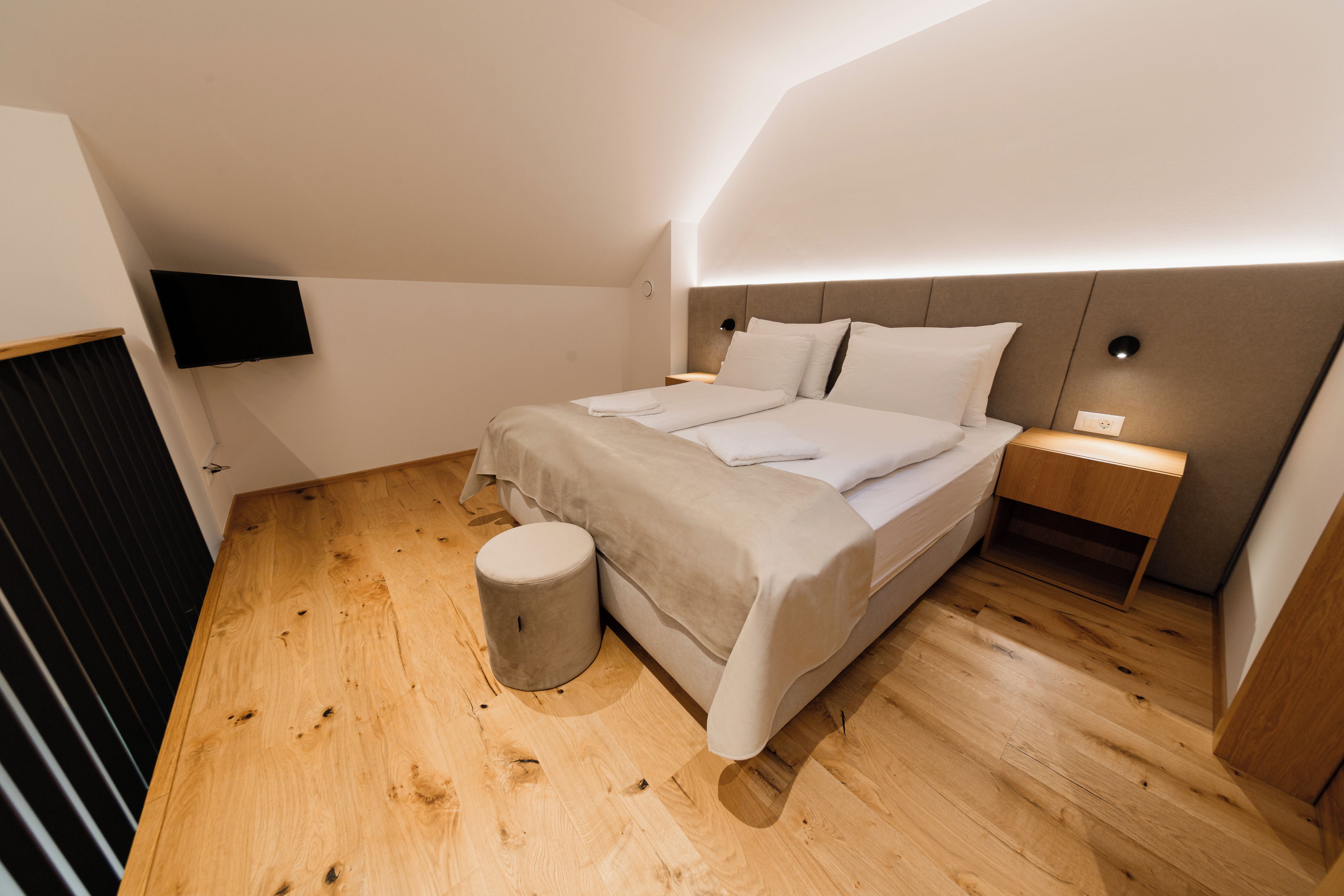 Un dormitorio moderno con cama, mesitas de noche, televisión y suelo de madera.
