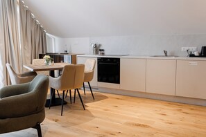 A modern kitchen with a dishwasher, a dining table with chairs, and a kitchen island with a sink. - Boutique Hotel Sončno Polje (Moravske Toplice)