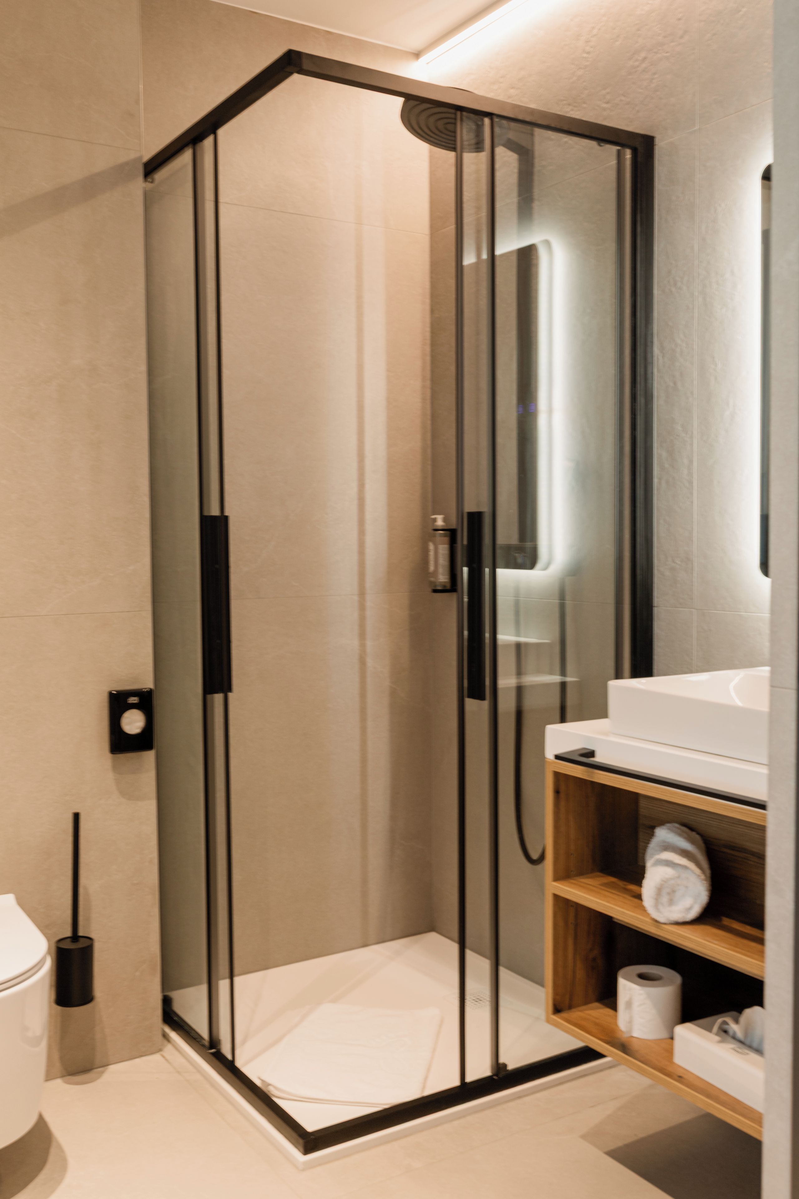 A modern bathroom with a glass-enclosed shower, a white sink, and a wooden shelf with toiletries.