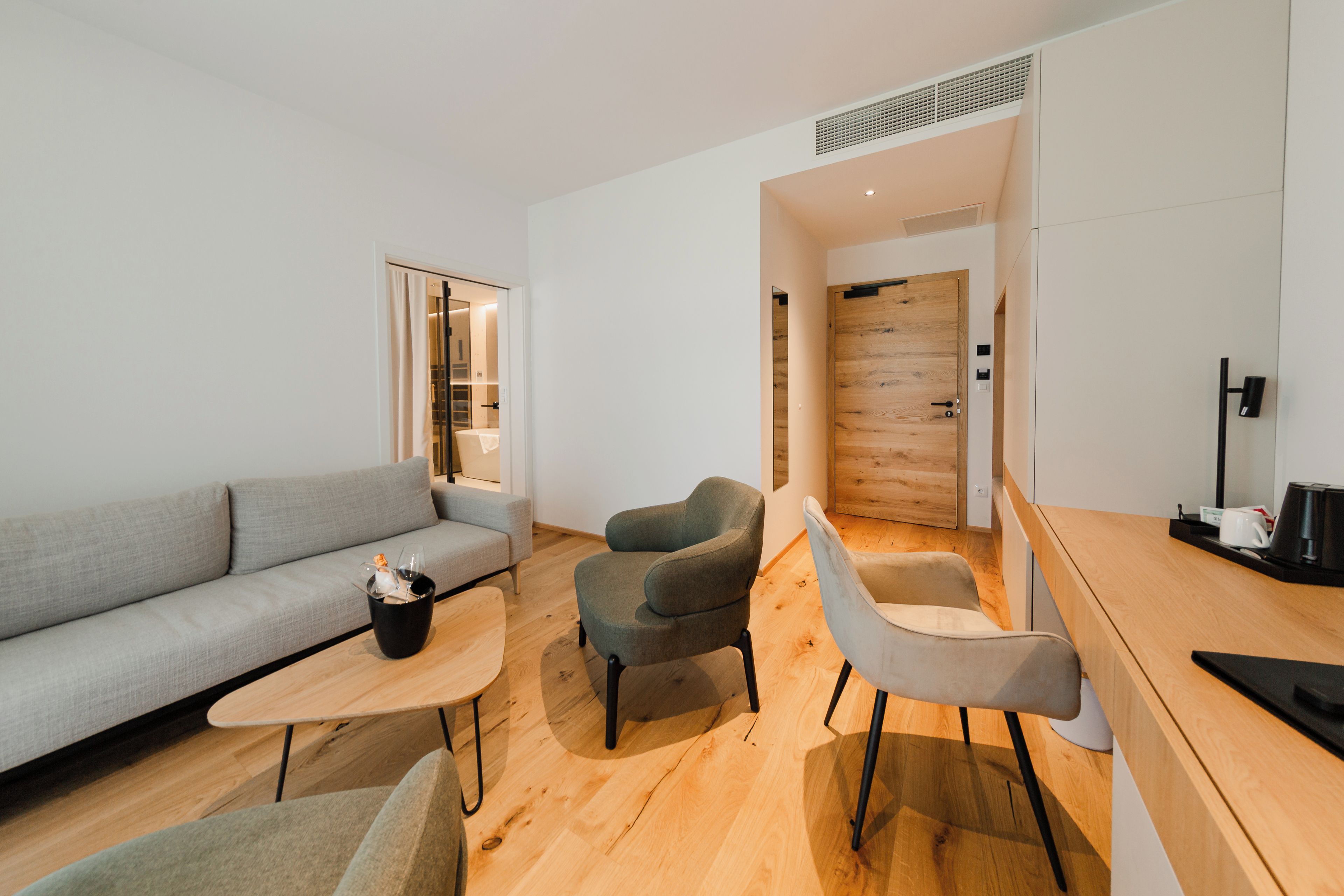 A modern living room with a grey sofa, two armchairs, a coffee table, and a wooden floor.