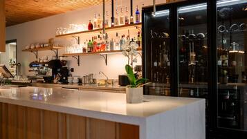 A bar area with a countertop, shelves with bottles, a coffee machine, and a refrigerator.