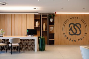 Una recepción de hotel con una computadora, sillas y una planta.