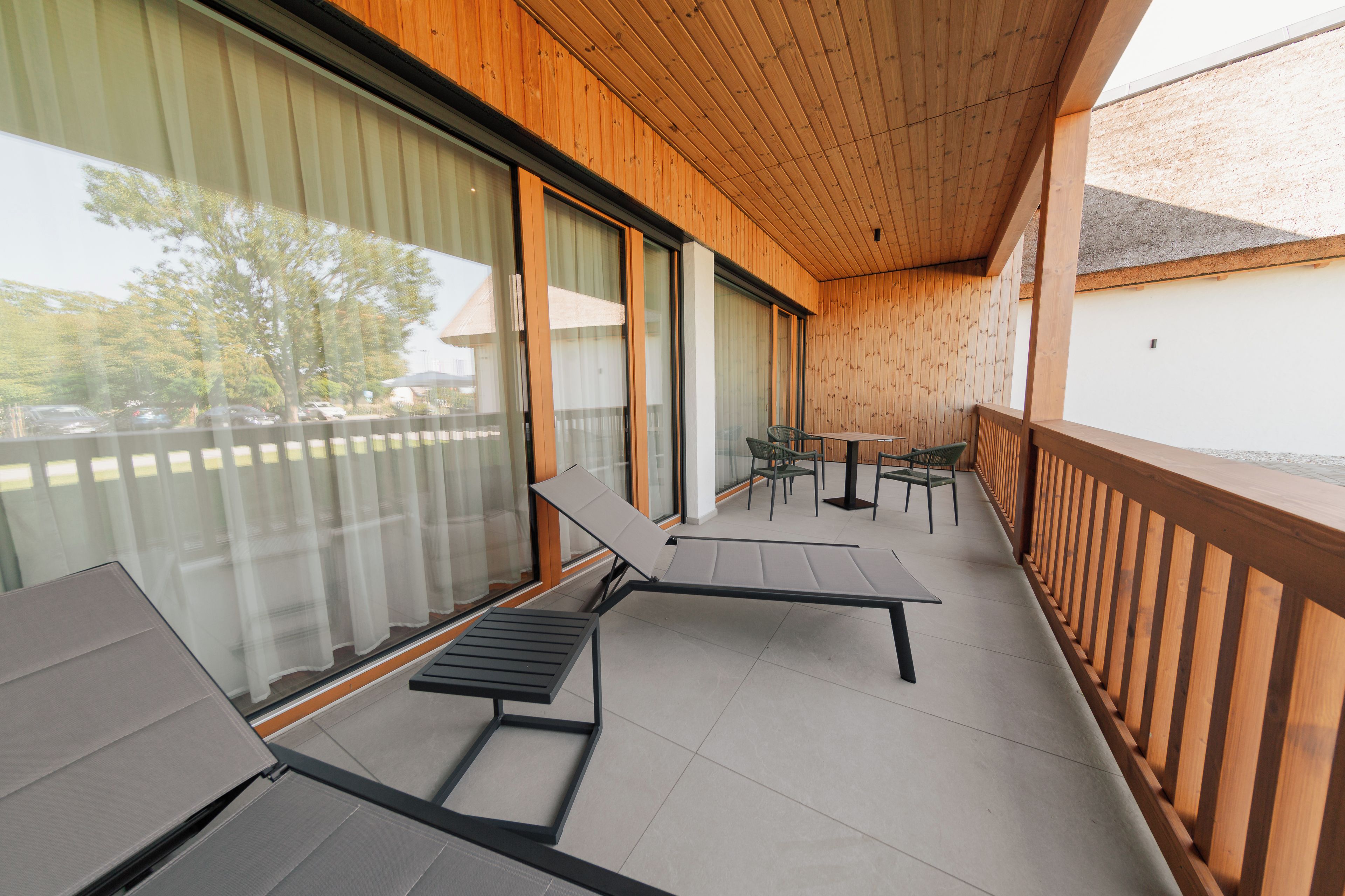 A balcony with two lounge chairs, a small table, and a view of a parking area.