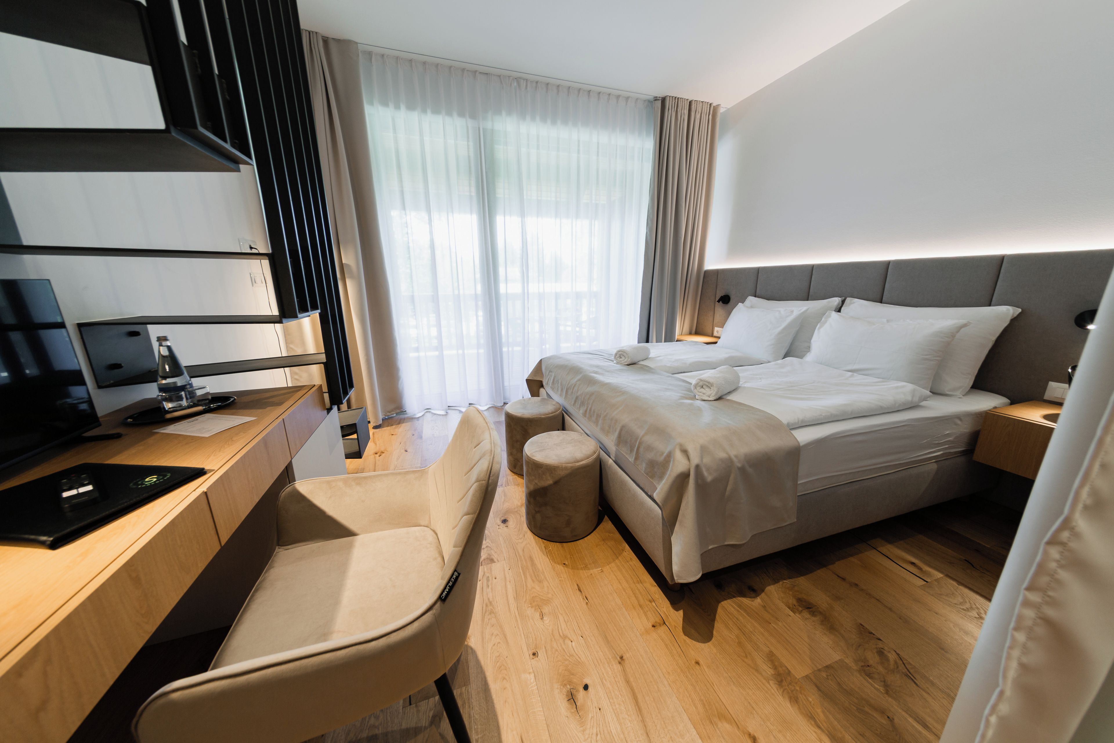 A modern hotel room with a bed, a desk, a chair, and a television.